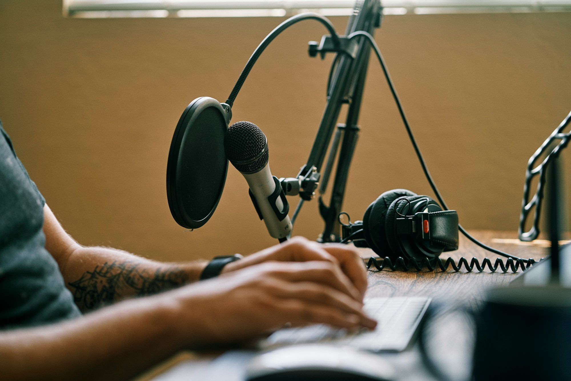 Hands typing on a keyboard at a desk beside a microphone with a pop filter and a pair of headphones.